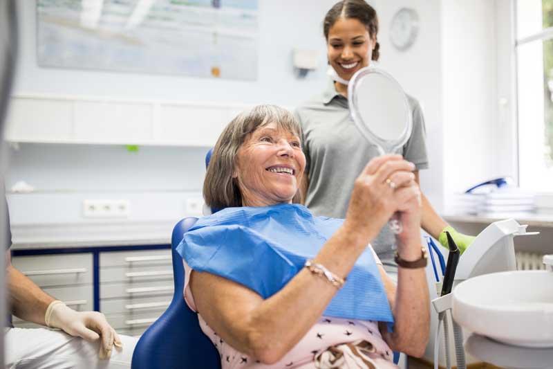 Senior kvinna som kollar sig i spegeln hos tandläkaren